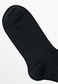 Schwarze Socke aus glattem, strukturiertem Stoff. Mit runder Zehenpartie und verstärktem Fersenbereich. Einfaches Design, keine Muster oder Akzente.