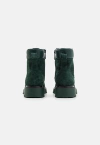 Bottines en suède vert avec une semelle en caoutchouc robuste, fermeture zippée sur le côté, et une finition textile pour un aspect texturé.