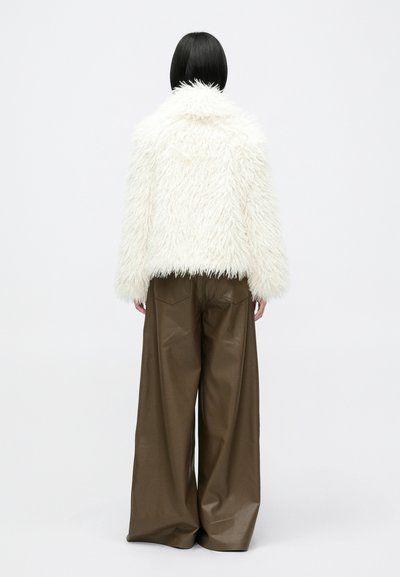 Biela umelá kožušina s golierom, v kombinácii s vysoko pásovými, širokými hnedými koženými nohavicami. Minimalistický dizajn, bez viditeľných log a vzorov.