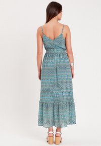 Robe maxi avec un motif géométrique bleu, vert et blanc, des bretelles spaghetti et un ourlet froncé. Le tissu semble léger et fluide.