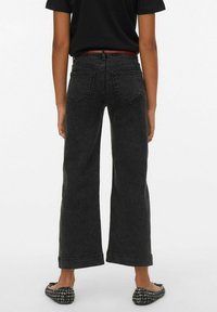 Svart, högmidjad jeans i denim med vida ben och rå kant, med bakfickor, kombinerade med svart topp och mönstrade flats.