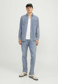 Svjetloplava traper košulja s копčama, dva dzepa na prsima, nosi se preko bijele majice i u kombinaciji sa svjetloplavim trapericama te ležernim tenisicama.