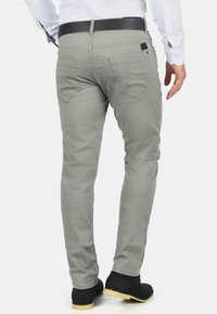 Gray cotton chinos feature a slim fit, back pockets with subtle stitching, and a black leather belt. The fabric has a smooth texture.