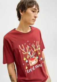 Rød bomulds t-shirt med et rensdyrgrafik, hvor gevirene er pyntet med farverige ornamenter, og teksten "Lad det sne" nedenfor.