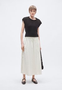 Μαύρο κοντομάνικο τοπ συνδυασμένο με λευκή φούστα με μαύρες πουά. Η φούστα έχει ελαστική μέση με κορδόνι και πλαϊνές τσέπες. Καφέ επίπεδα παπούτσια.