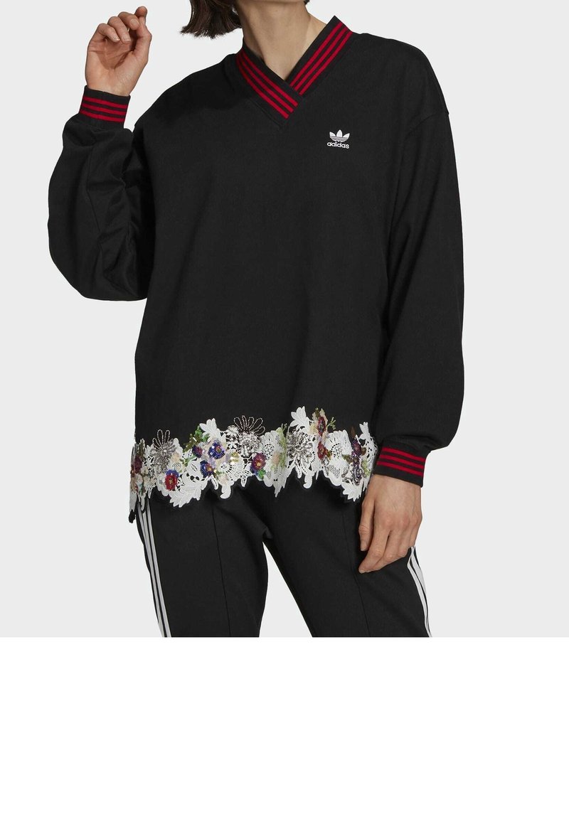 Mustapaita, jossa on V-pääntie, punaraitainen kaulus ja valkoinen kukkakuvioinen pitsi helman kohdalla. Paitassa on pieni Adidas-logo rinnassa.