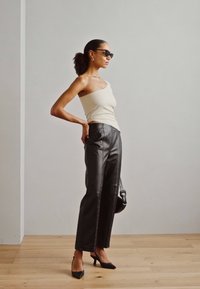 Melna ādas platajām biksēm ar baltu šuvumu, kombinētām ar krēmīgas krāsas bezpiedurkņu topu un melniem stiletto papēžiem. Aksesuāri ietver saulesbrilles.