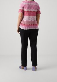 Pletený top s vzorem v žinovém stylu v růžové a bílé barvě, spárovaný s černými kalhotami a levandulovými botami na blokovém podpatku, pohled zezadu.