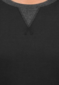 Sudadera negra con cuello redondo gris contraste y detalle en pico texturizado. Fabricada en una suave y elástica tela. Sin patrones visibles ni herrajes.