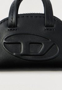 Κοντινή λήψη από μαύρη δερμάτινη τσάντα χειρός που δείχνει το ανάγλυφο οβάλ λογότυπο και τις ραμμένες λαβές σε απλό φόντο.