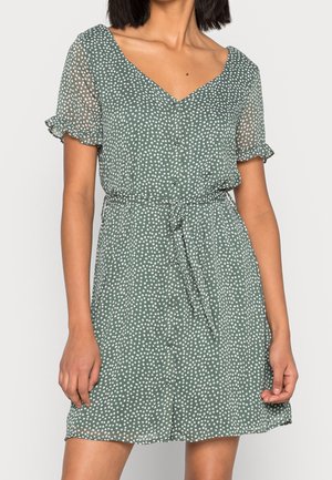 Robe courte verte à pois blancs, décolleté en V, manches transparentes, taille froncée et un lien à la taille. Tissu léger.