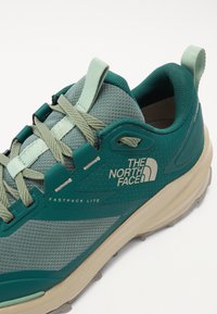 Teal and mint sneaker with mesh upper, lace-up closure, and rubber sole. "The North Face" logo and "Fastpack Lite" text featured.