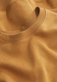 Gros plan d'un pull en maille jaune moutarde plié montrant un col rond côtelé et une texture de tissu lisse.