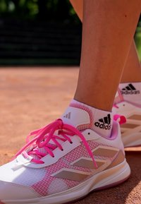 Athletic shoes with a white and pink textile upper, featuring pink laces and three silver stripes. Accented with a pink sole and logo.