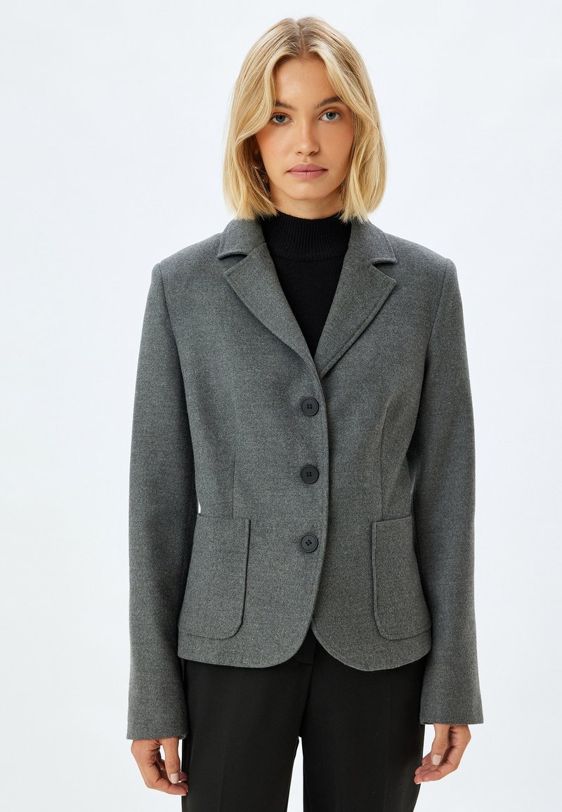 Grijze wolblend blazer met geknipte revers, drie zwarte knopen, twee voorzakken en een getailleerde pasvorm. Lange mouwen, zachte textuur.