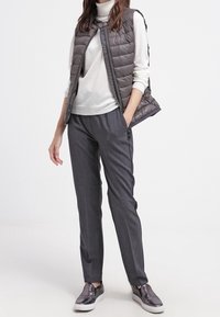 Gilet imbottito grigio sopra un dolcevita bianco, abbinato a pantaloni grigi e scarpe slip-on texture. Design semplice con dettagli funzionali.