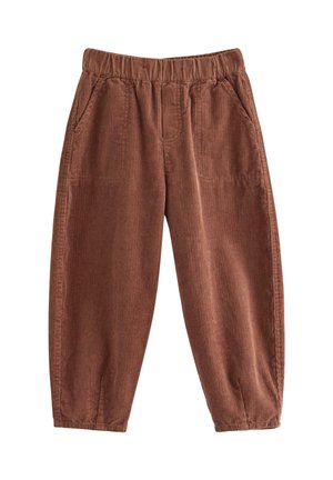 Unge dreng justerer navyblå hat, iført en blå langærmet skjorte med bjørnemærke, brune fløjlsbukser og grønne sneakers, står på hvid baggrund.
