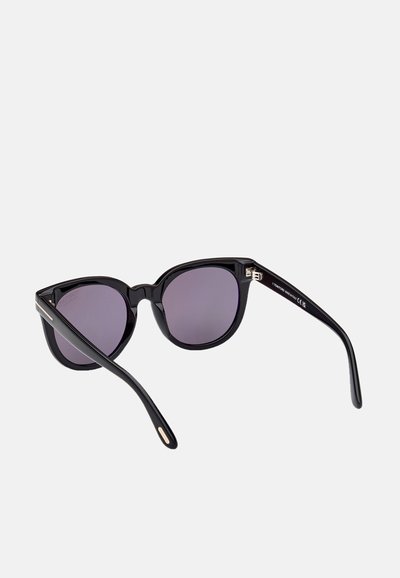 Des lunettes de soleil style œil de chat avec des montures noires et des verres teintés en violet. Elles présentent des bords incurvés élégants et de fins accents métalliques sur les branches.