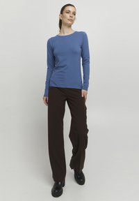 Langärmliges blaues Oberteil aus weichem Stoff, kombiniert mit weiten braunen Hosen. Das Outfit hat einen runden Ausschnitt und eine figurbetonte Silhouette.