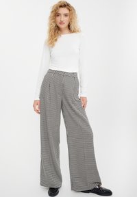 Czarno-białe spodnie w wzór houndstooth o szerokich nogawkach i wysokim stanie, połączone z gładką białą bluzką z długim rękawem. Gładka tekstura materiału.