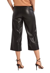 Pantalons cropped en simili cuir noir avec taille haute, poches latérales et jambes larges. Présente une texture brillante et un détail de couture sur l'ourlet.
