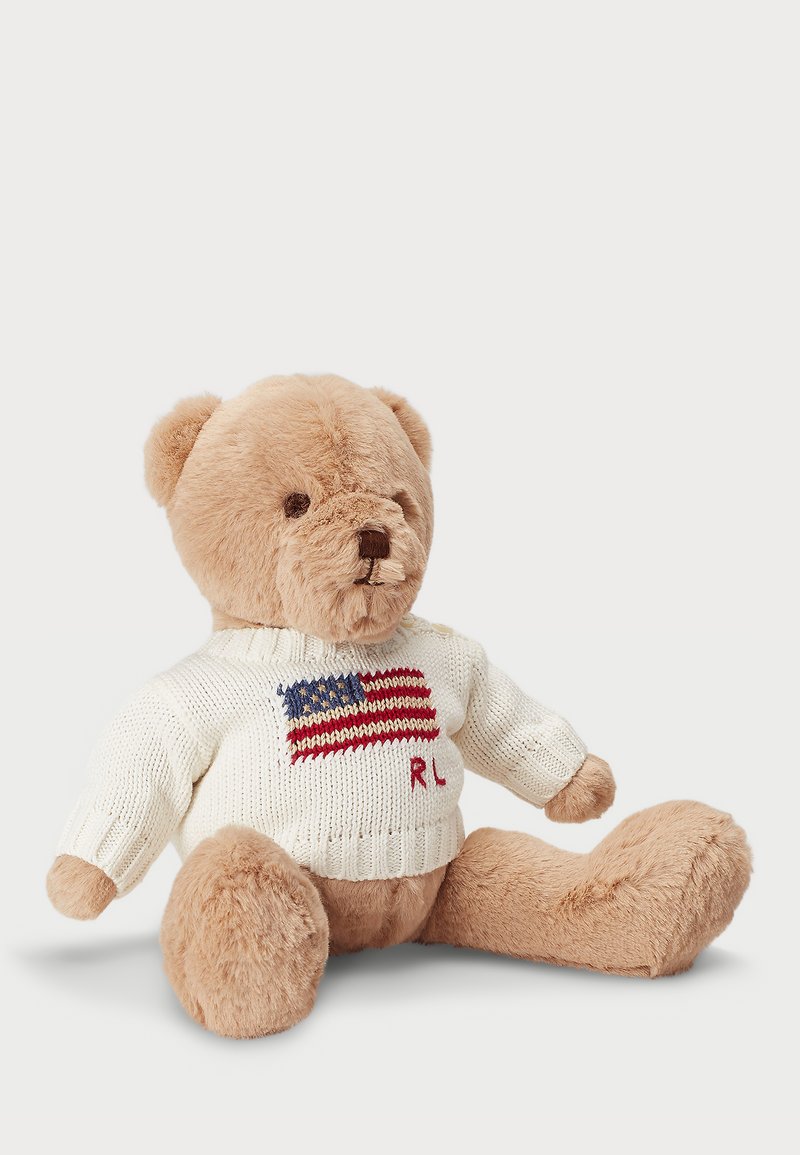 Lācīts, kas izgatavots no mīkstas beige krāsas kažokādas, valkā krēmas krāsas džemperi ar sarkano un zilo Amerikas karogu, un uz priekšpuses ir izšūts "RL".