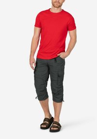 Red short-sleeve t-shirt, paired with knee-length dark gray cargo pants featuring pockets and a subtle pattern, worn with brown sandals.