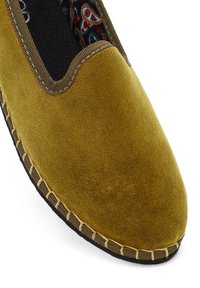 Żółte zamszowe klapki z brązowym wykończeniem i widocznym szwem na czarnej podeszwie, z wzorzystą tkaniną w środku.