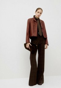 Giacca cropped bordeaux, camicia nera, pantaloni larghi a quadri marroni e una borsa scura a tracolla. Texture in pelle liscia con dettagli di cucitura discreti.