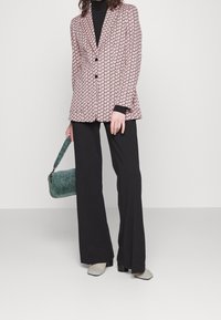 Vzorovaný blazer v růžové a černé barvě, doplněný černými širokými kalhotami a šedými botami. Zelená kabelka přidává kontrast. Hladká textilie.