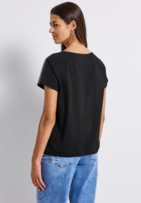 Zwart top met korte mouwen en een ronde hals, met mesh accentueringen op de schouders. Gecombineerd met lichtblauwe denim jeans.