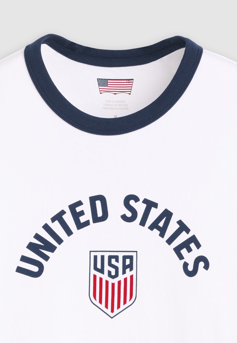 White t-shirt with navy collar, "UNITED STATES" text arched above a shield logo reading "USA" with red vertical stripes.
