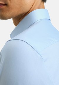 Light blue shirt with a textured fabric, featuring a structured collar and neat stitching along the shoulder seam.