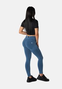 Siniset denimhousut, joissa on korkeavyötärö ja kapeat lahkeet. Kangas on sileää, ja housuissa on takatasku sekä pieni logo. Mustat lenkkarit täydentävät asun.