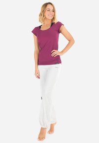 Lila, enganliegendes T-Shirt mit kurzen Ärmeln, kombiniert mit locker sitzenden, weißen Hosen mit elastischen Bündchen und einem schwarzen Logo-Patch an der Hüfte.