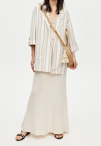 Striped beige and white oversized blazer over a cream knit maxi skirt, paired with black sandals and a textured straw bag.
