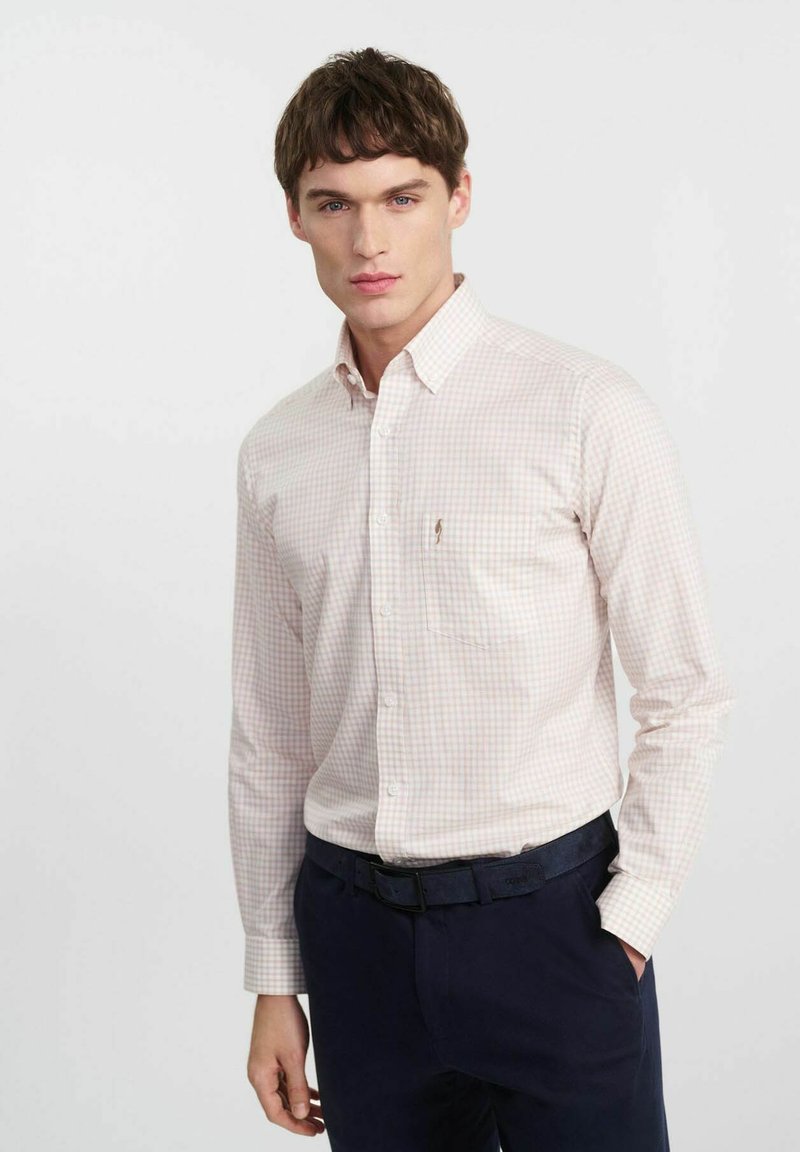 Jasnoróżowa koszula w kratkę z długimi rękawami, kołnierzykiem, z zapięciem na guziki z przodu i małym logo na piersi, zestawiona z ciemnonawigacyjnymi spodniami i czarnym paskiem.