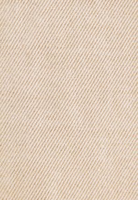 Gros plan sur la texture d’un tissu à rayures diagonales beige et blanc cassé avec des fils tissés visibles.