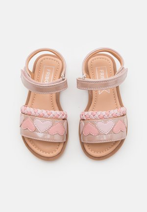 Sandali rosa con cinturino intrecciato a forma di cuori, finitura lucida e cinturini alla caviglia regolabili. Suole lisce con solette di colore chiaro.