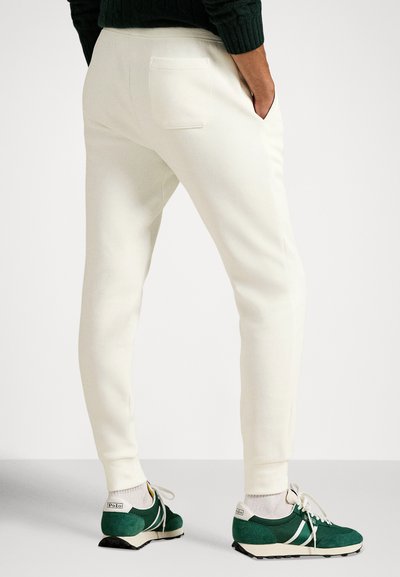 Λευκή φόρμα με εφαρμοστή γραμμή, με πίσω τσέπη. Συνδυασμένη με πράσινα αθλητικά παπούτσια και ανοιχτόχρωμες κάλτσες. Λείο ύφασμα.