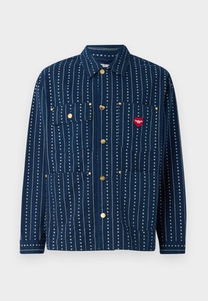 Veste bleu marine à boutons, avec des rayures blanches verticales, deux poches poitrine, des boutons dorés, et un patch logo cœur rouge sur la poche droite.