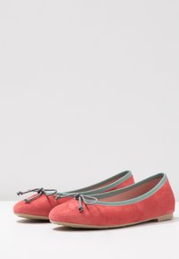 Korallfärgade mocka ballerinaskor med rund tå, grön kant och grå rosettdetalj framtill. Platt beige sula.