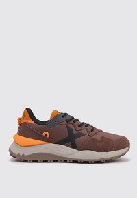 Chaussures de sport brunes avec des accents orange, un logo noir, une tige texturée, une semelle rembourrée et un profil robuste pour une meilleure traction.