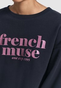 Felpa navy con stampa metallica rosa che recita "french muse one step 1995". Design classico con collo a giro e bordo ribattuto.