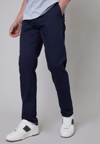 Chinos bleu marine à coupe slim, en tissu de coton lisse, dotés de poches latérales. Associés à des baskets blanches avec des détails en vert.