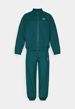 Tyrkysový teplákový komplet pozostávajúci z mikiny na zips a zodpovedajúcich nohavíc s elastickými manžetami. Na mikine a nohaviciach sa nachádza logo.