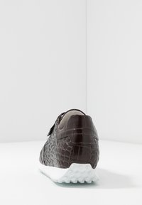 Sneaker en cuir de crocodile marron foncé avec une semelle en caoutchouc blanche, dotée d'une sangle velcro et d'un design de talon arrondi.