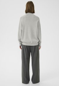 Maglione grigio chiaro con collo alto e spalle cadenti, abbinato a pantaloni larghi grigio scuro. Texture morbida, vestibilità casual.