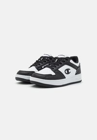 Sorte og hvide sneakers med læder overdel, der har en perforeret tåboks, flade snørebånd og et brandet logo på siden. Struktureret gummisål.