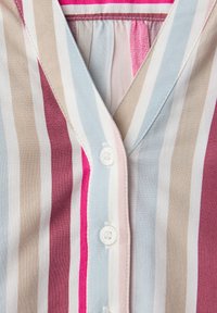 Gros plan sur le devant d'une chemise boutonnée à rayures verticales beige, bleu clair, rose, blanc et bordeaux.